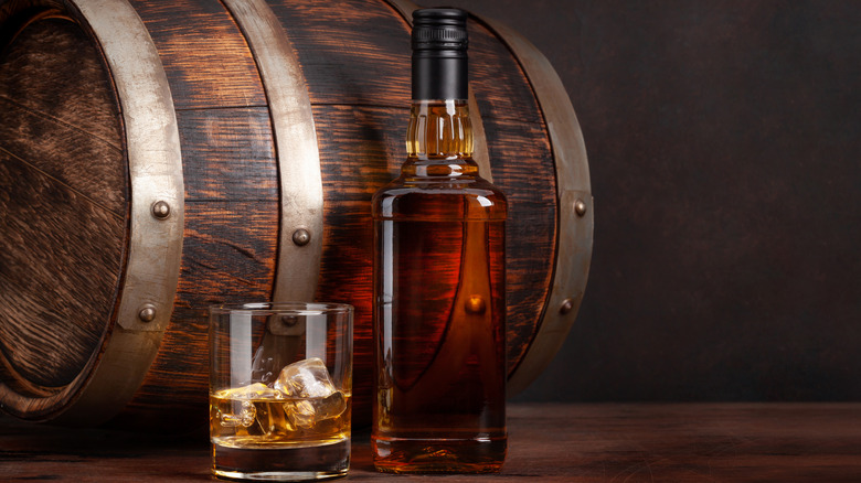 Glass and bottle of whiskey beside barrel