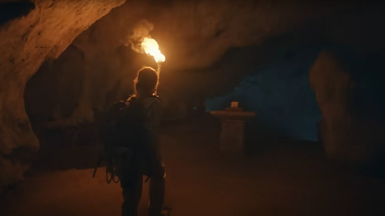 Woman holding torch approaching artifact in cave in Live from PS5 ad