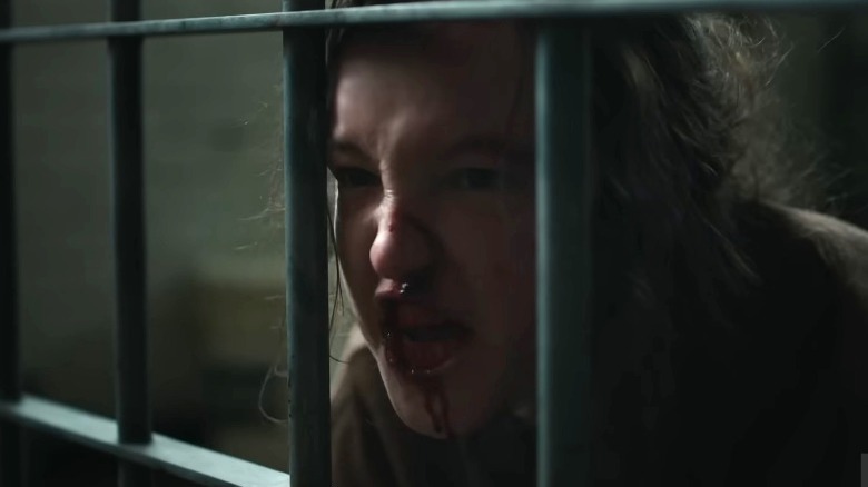 Ellie yelling with bloody mouth behind prison bars