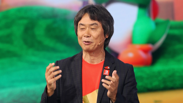 Shigeru Miyamoto talks to a crowd in front of a Yoshi backdrop
