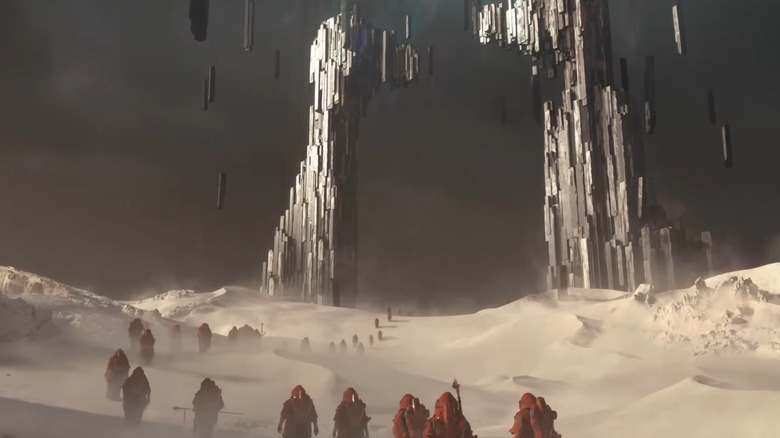 Red clothed figures walking through desert to huge structure