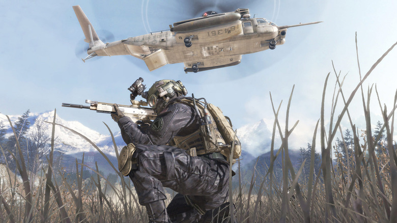 Operator kneeling and aiming in grass with a helicopter overhead