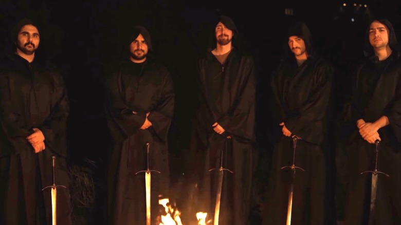 OTK members in robes holding swords in front of fire