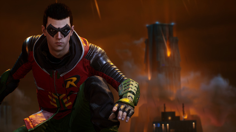 A screenshot from Gotham Knights, showing Robin crouched in the foreground. Behind, a tower is engulfed in flames.